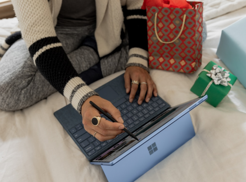 Femme travaillant sur un ordinateur portable Surface sur un lit entourée de cadeaux.