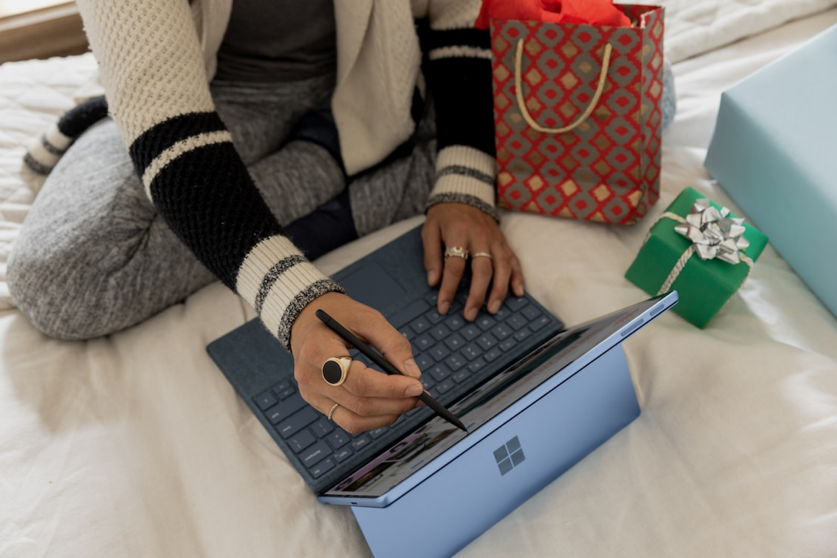 Femme travaillant sur un ordinateur portable Surface sur un lit entourée de cadeaux.