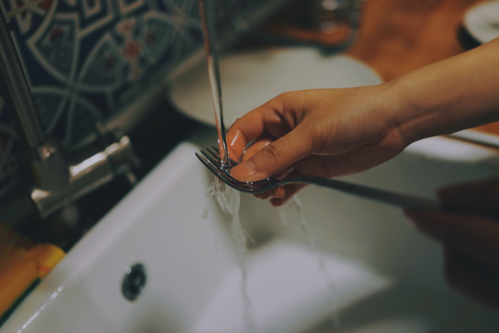 Une personne tenant une fourchette au-dessus d'un évier avec de l'eau qui coule.