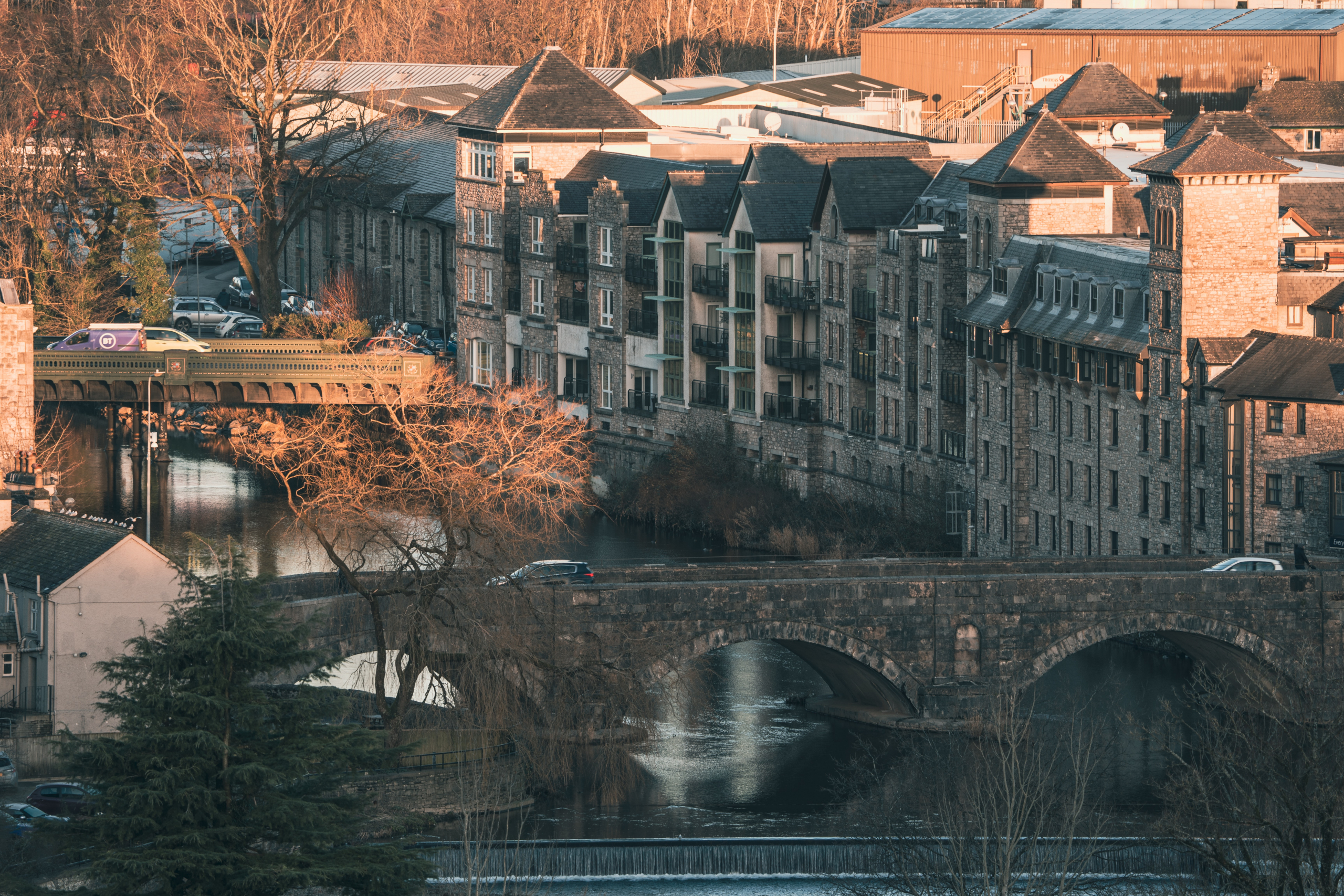 Vue urbaine d'un pont en pierre au-dessus d'une rivière entourée de maisons.