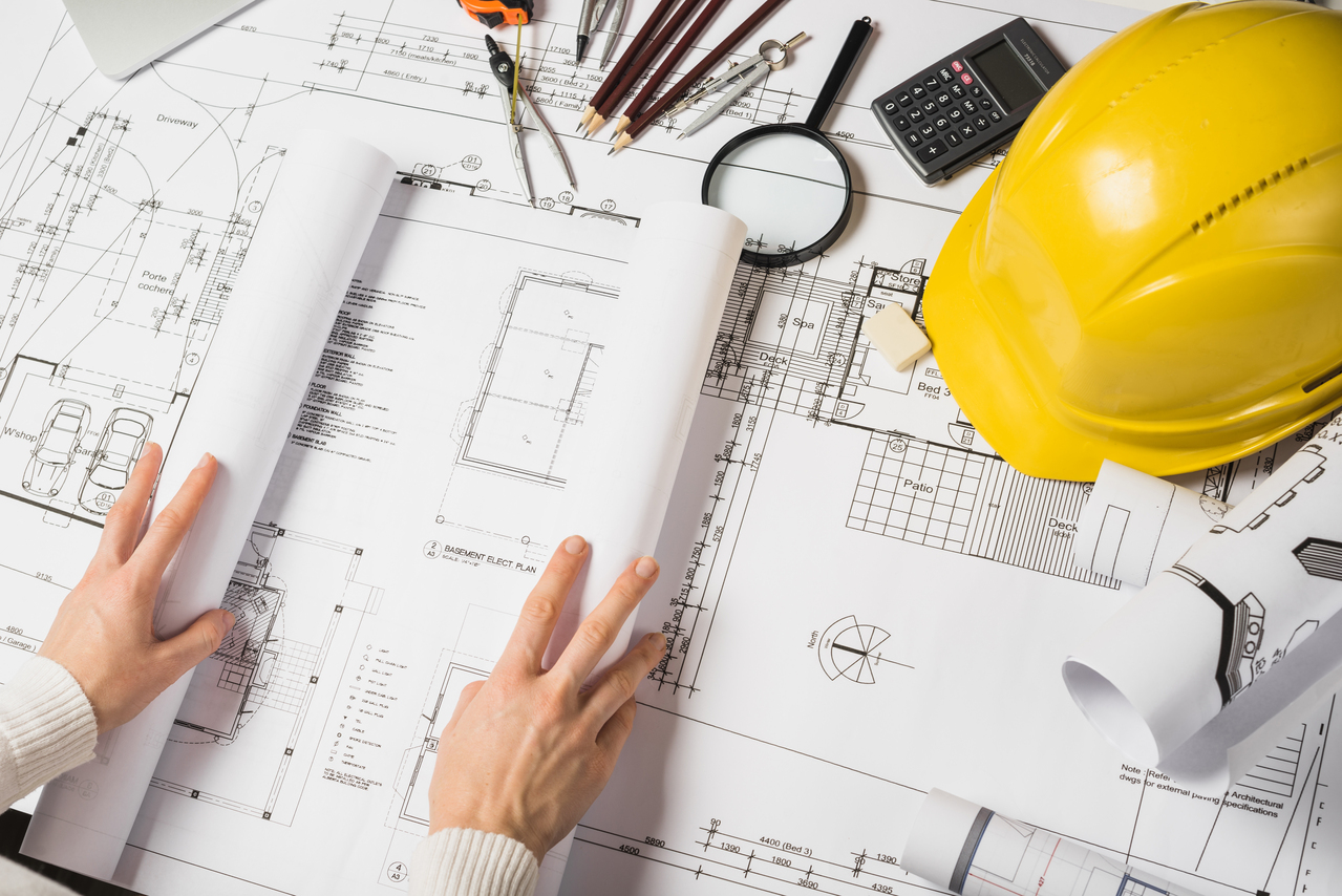 Les mains d'une personne sont posées sur un plan et un casque de chantier.